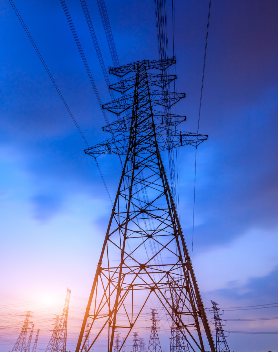 A high-voltage transmission tower seen from below against an evening sky, with more pylons in the distance
