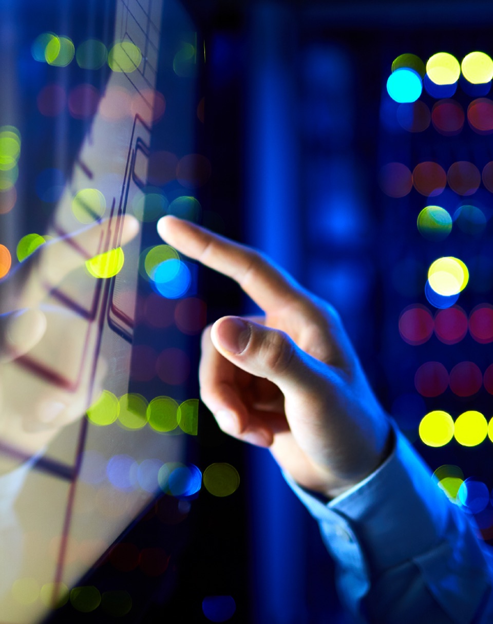 A hand reaching towards a touchscreen in a data centre, with server lights glowing in the background